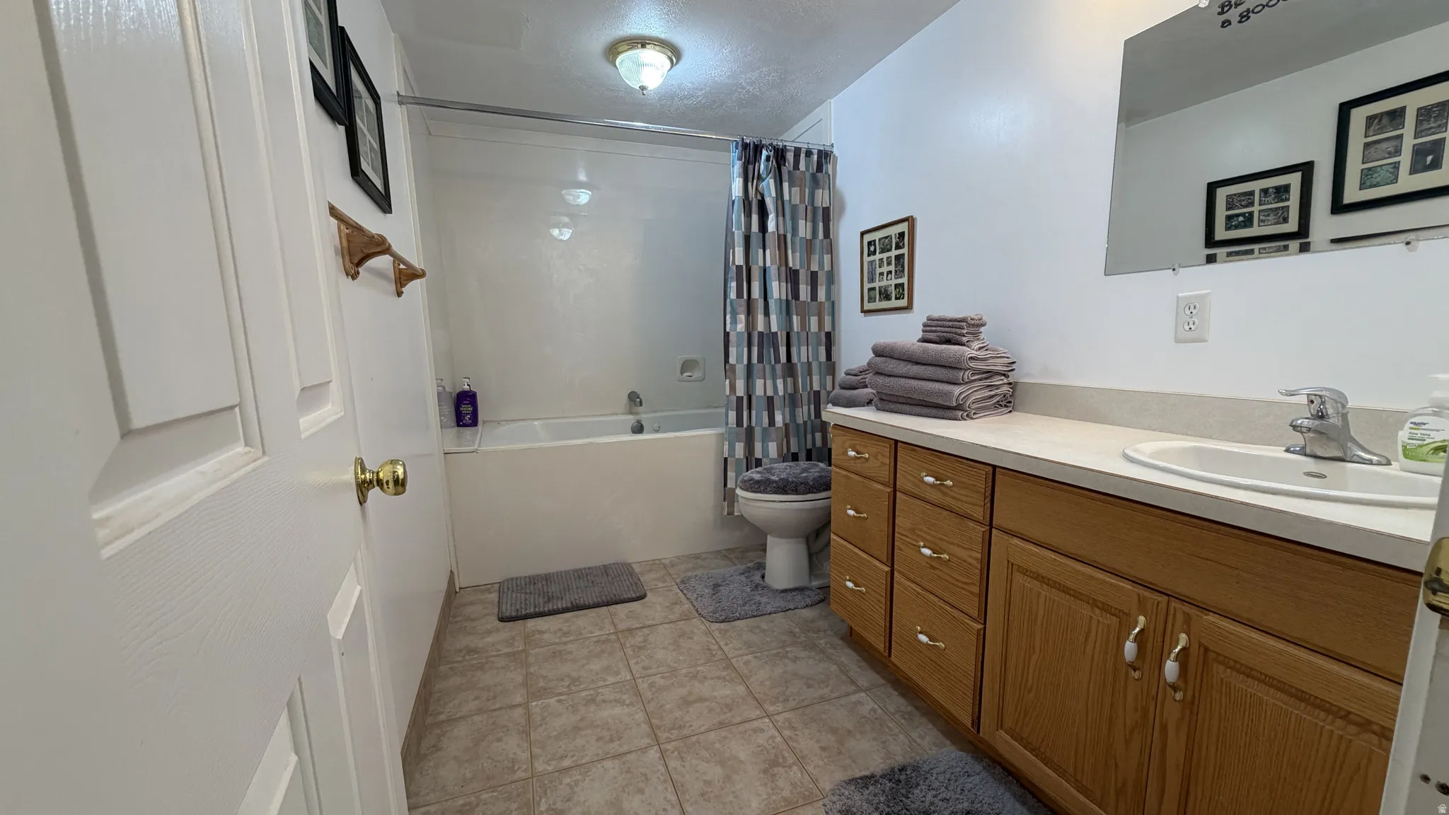 Full bathroom featuring a single vanity with wood-finish cabinetry, a built-in bathtub with shower, and tile flooring