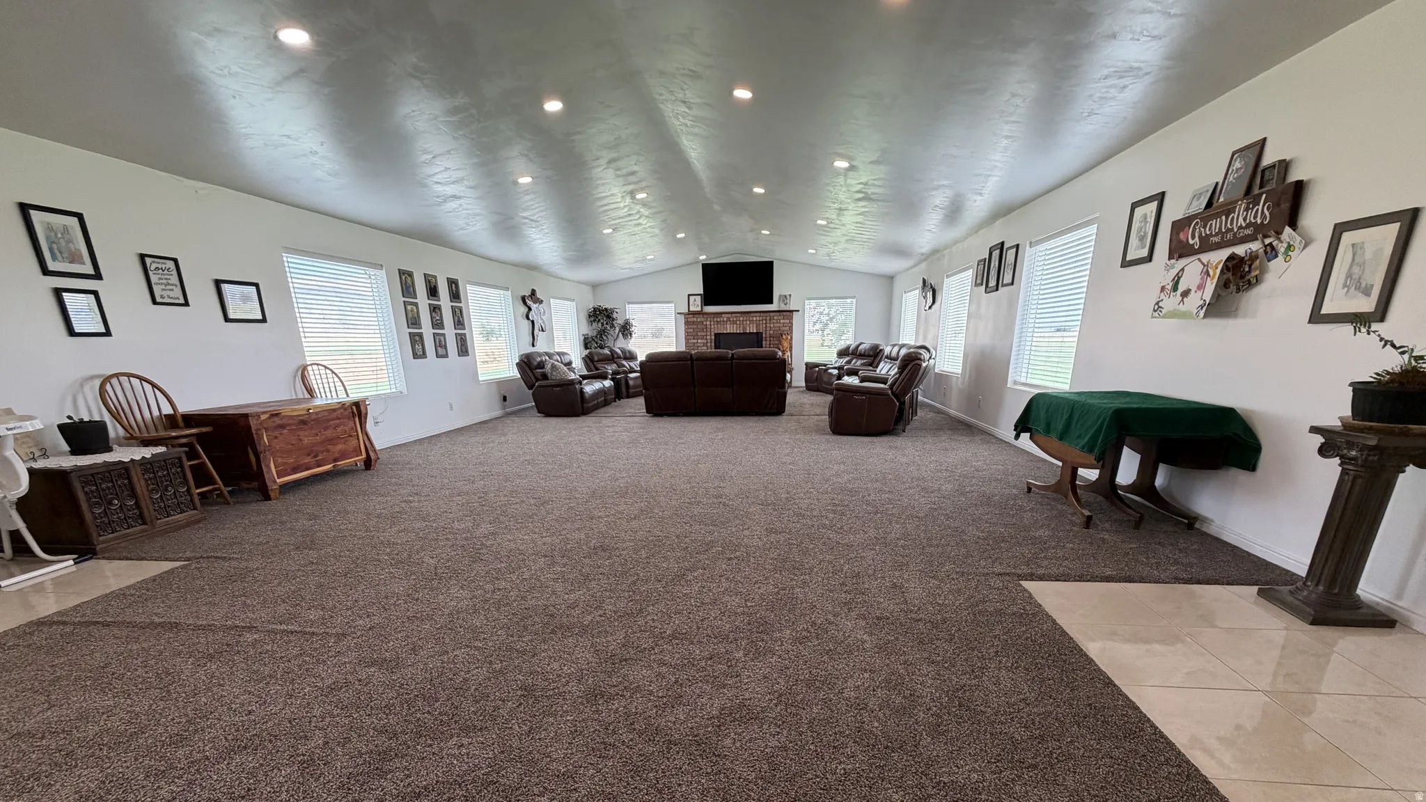 Spacious gathering room with recessed lighting, multiple windows, a stone-faced fireplace, and mixed flooring
