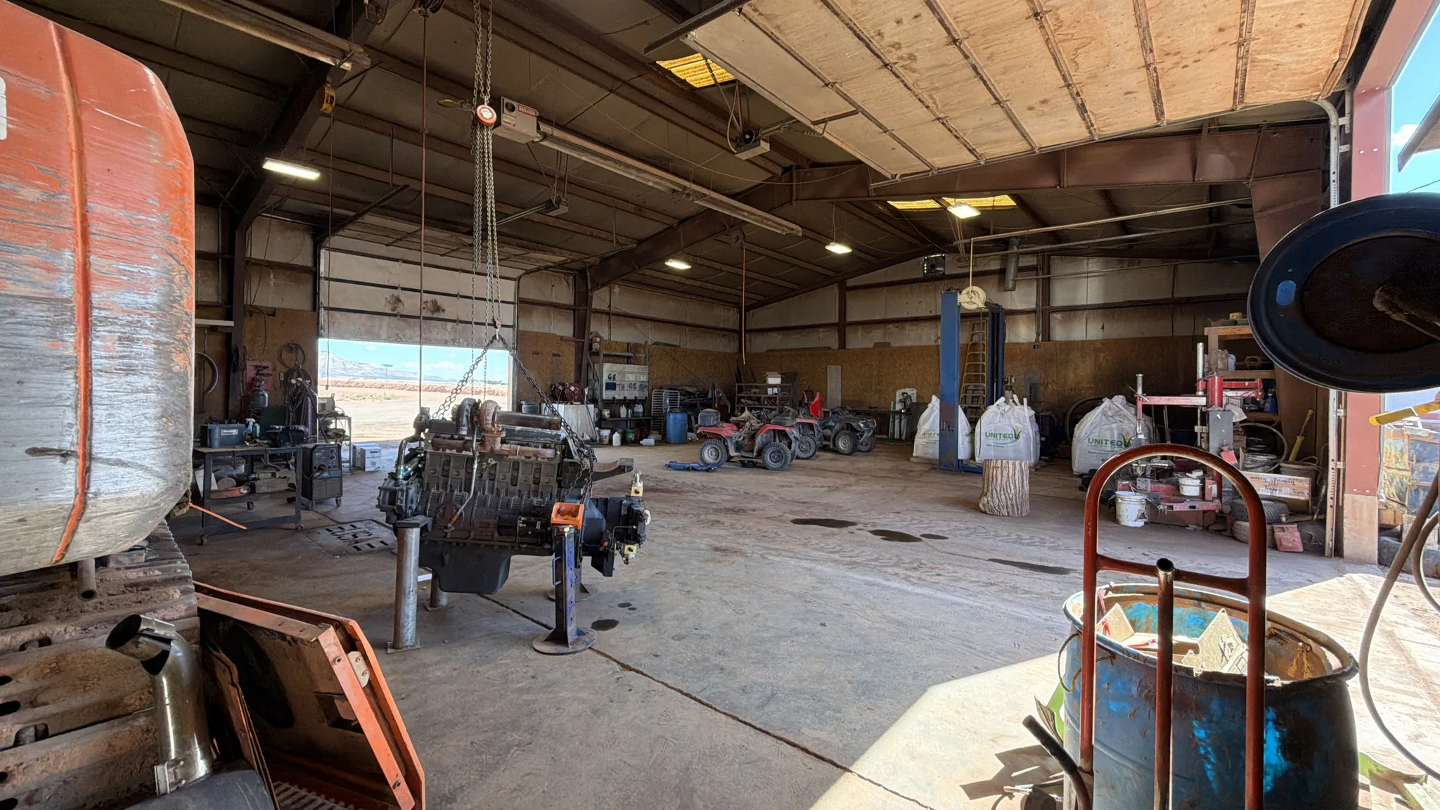 Spacious workshop featuring concrete flooring, multiple overhead doors, and high ceilings with exposed structural beams