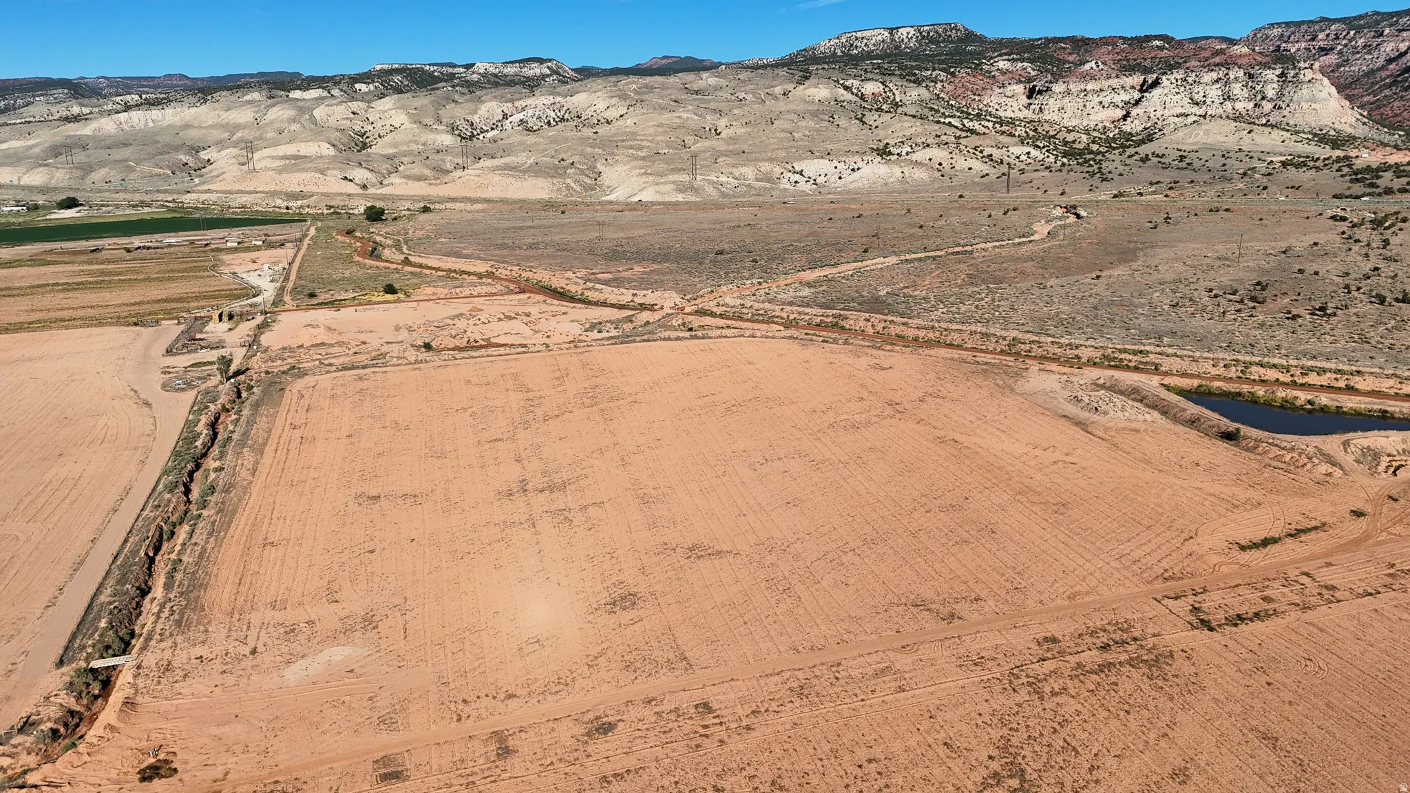 Expansive land parcel with graded terrain, a visible water feature, and distant mountainous topography