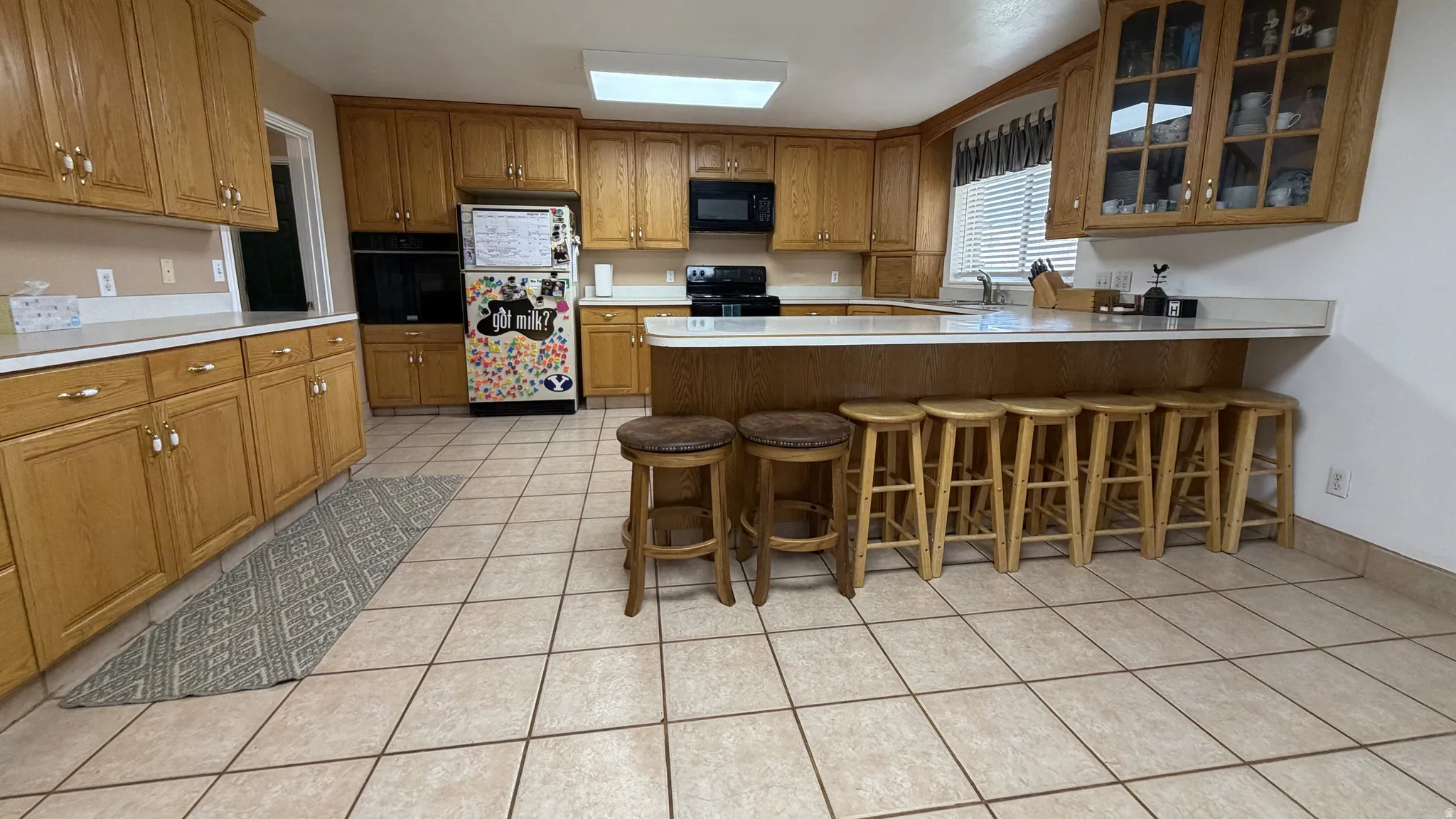 Kitchen featuring extensive wood cabinetry, light-toned countertops, tile flooring, built-in wall oven, and a breakfast bar