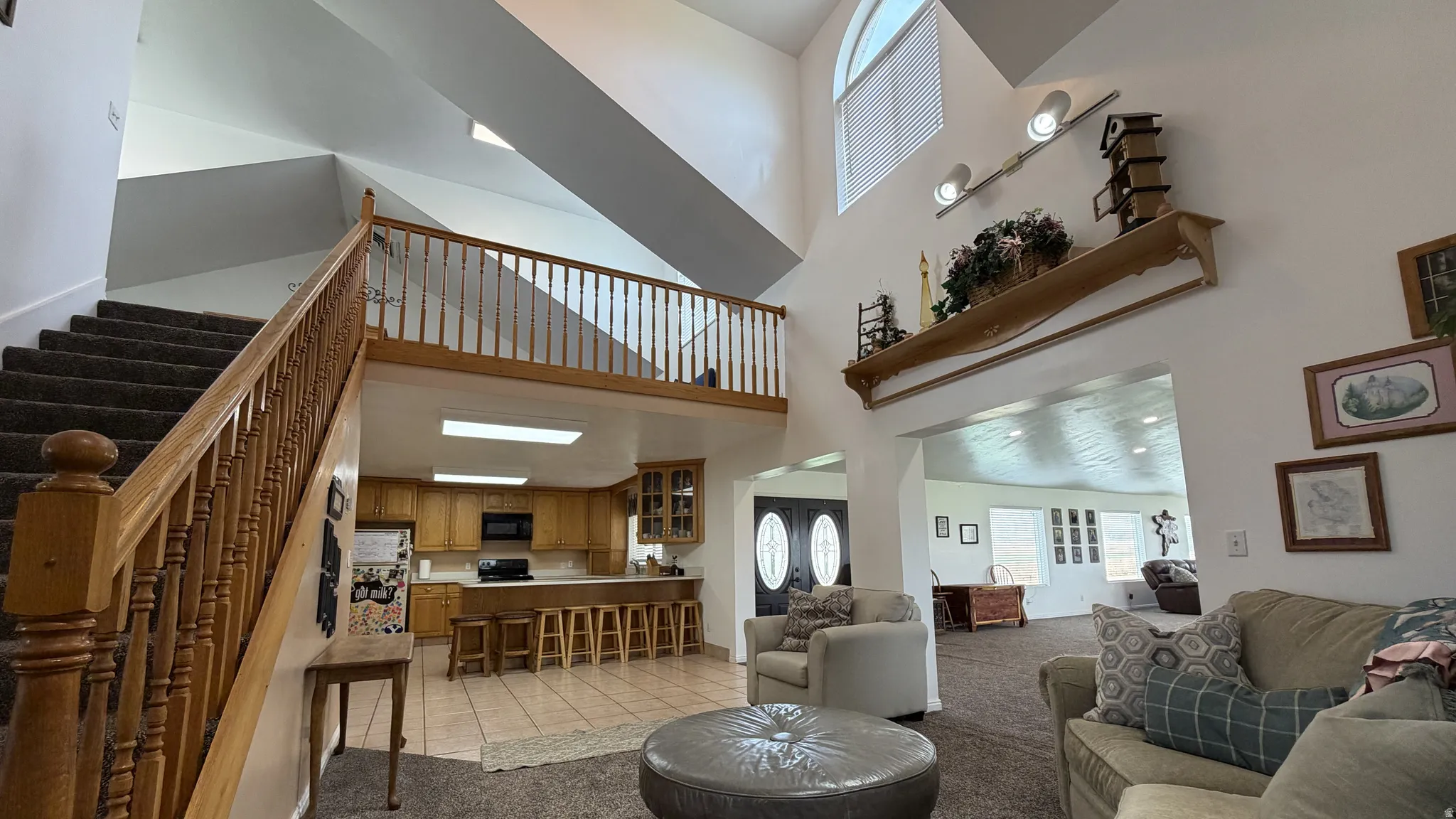 Two-story living area with high vaulted ceilings, an open mezzanine, natural wood railing, and a functional kitchen with wood cabinetry