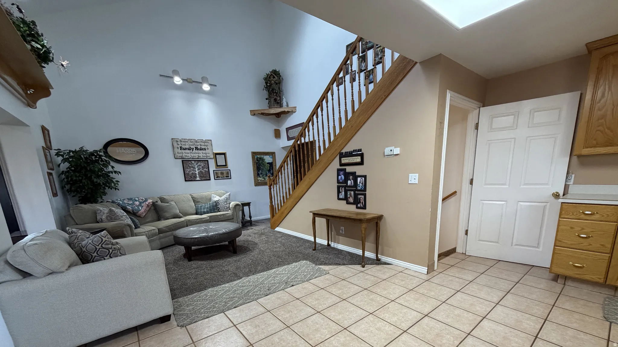 Vaulted ceiling, open-tread staircase with wood railing, recessed ceiling light, wood-finish cabinetry, and tile flooring