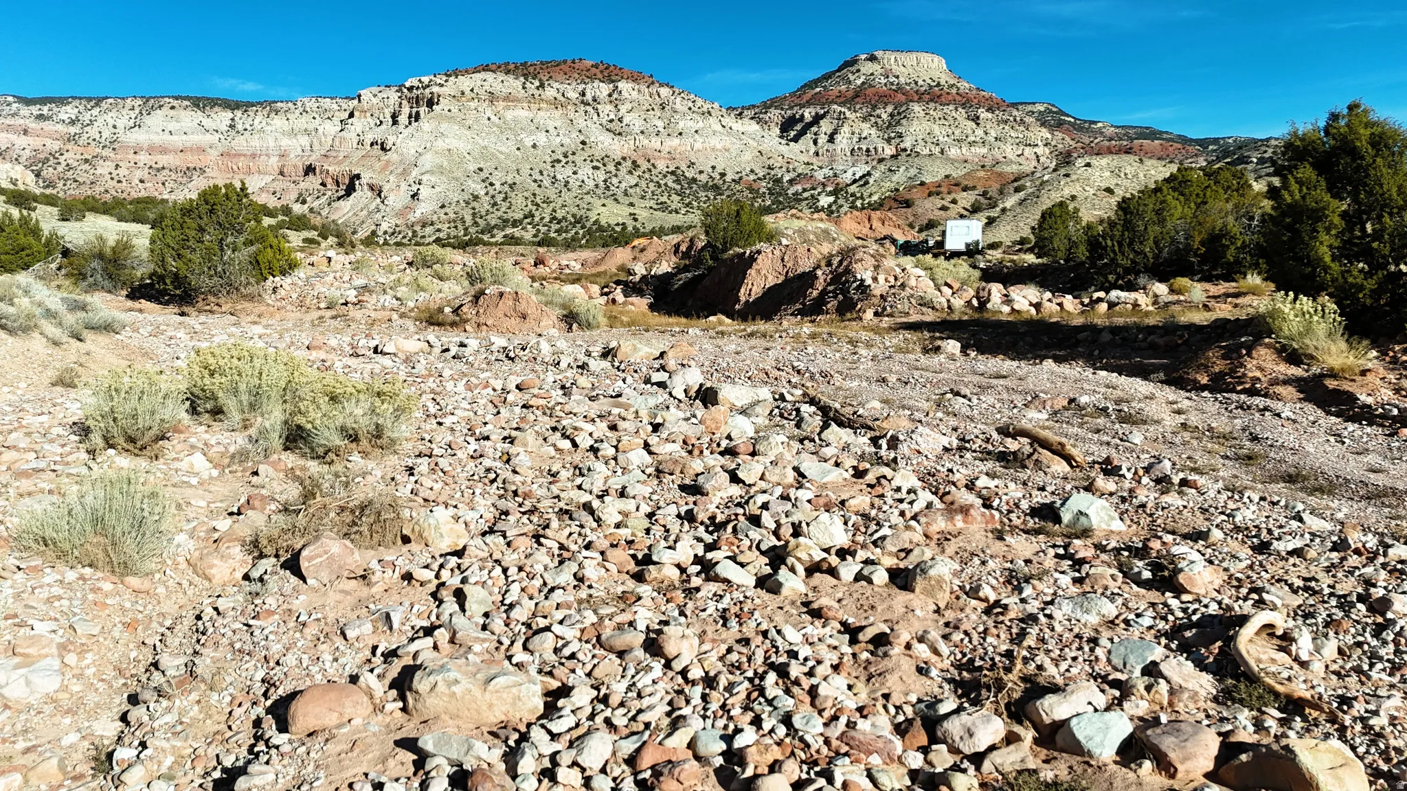 Expansive lot with distant layered rock formations, scattered brush, and a clear blue sky