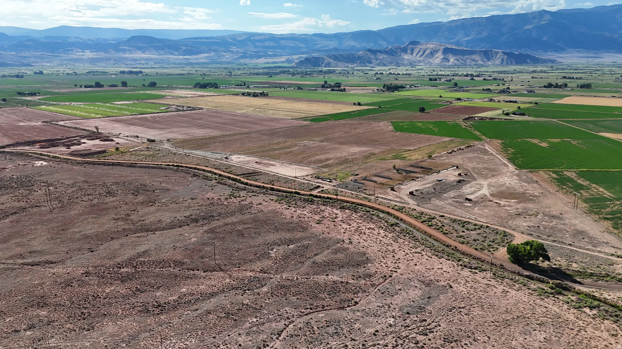 Expansive land parcel featuring a dirt road, mature trees, and mountainous terrain in the distance