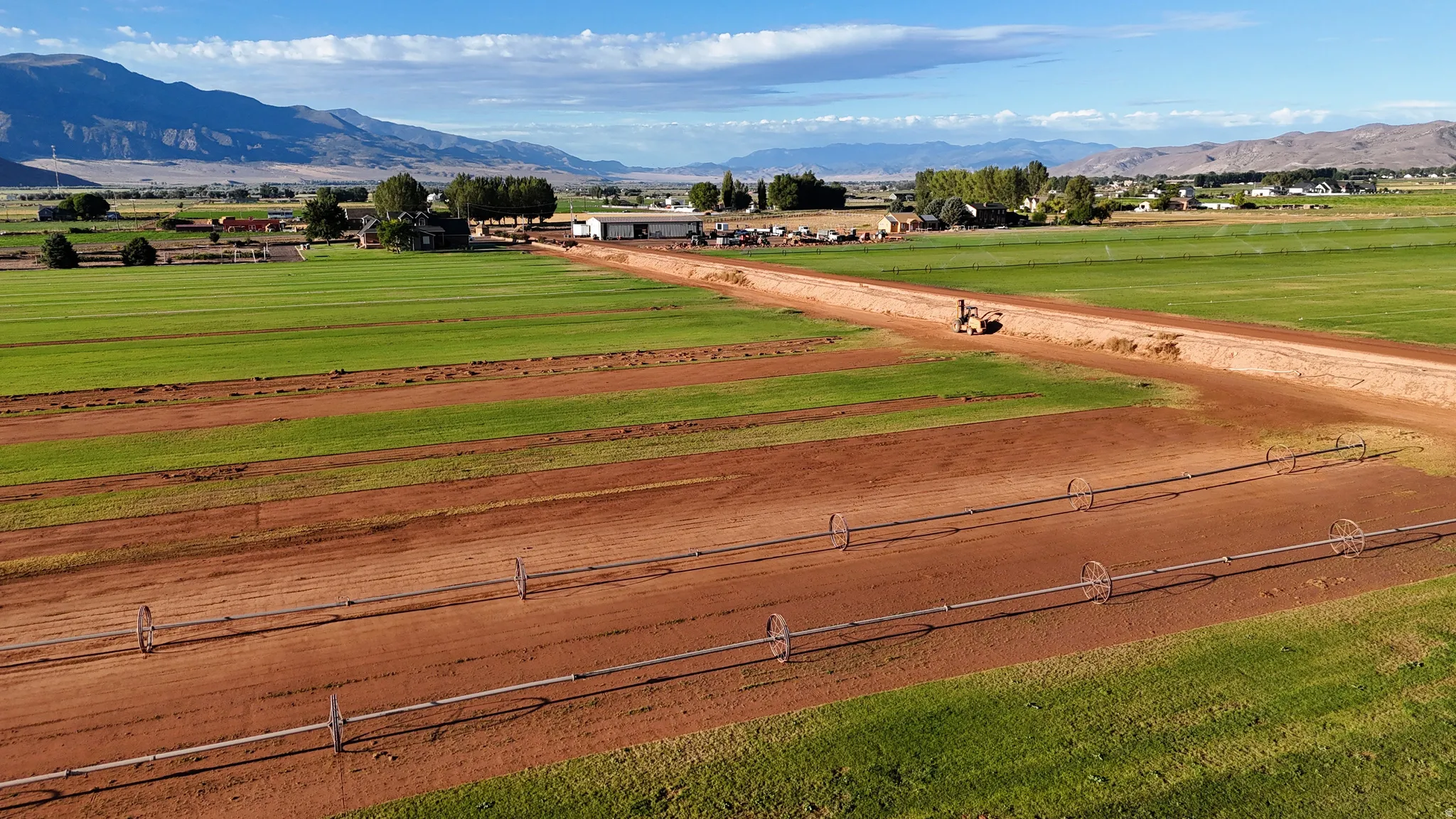 Expansive agricultural land featuring a system of irrigation lines, partially cultivated fields, and distant mountain scenery