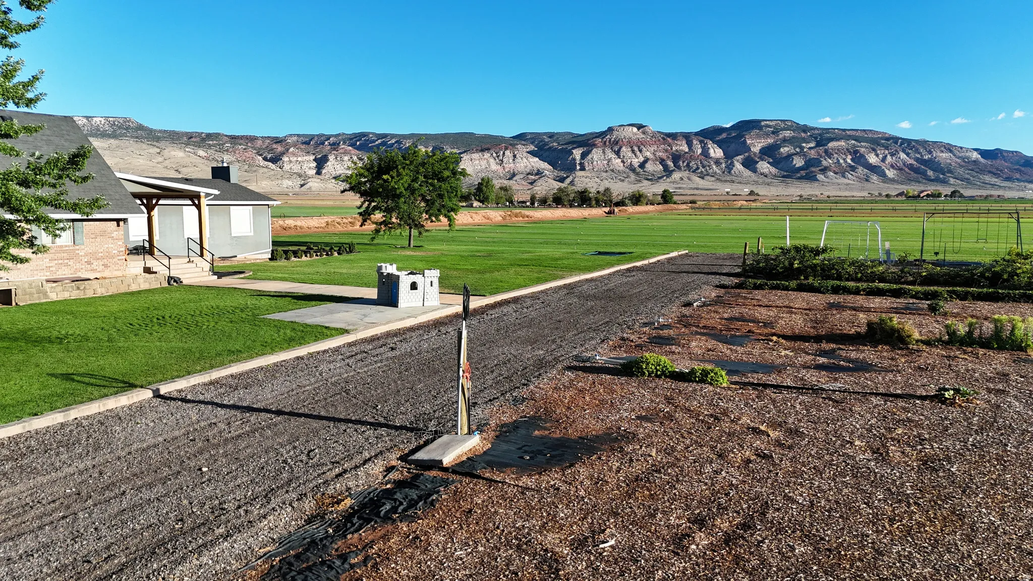 Expansive property featuring a gravel driveway, lush green lawn, distant mountain range, and a covered porch entry