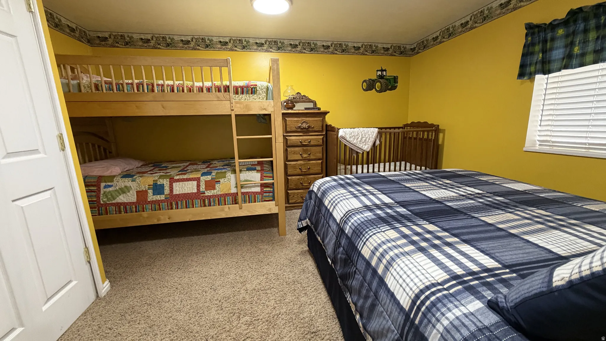 Carpeted room with a wooden bunk bed, a wooden crib, and a wooden dresser