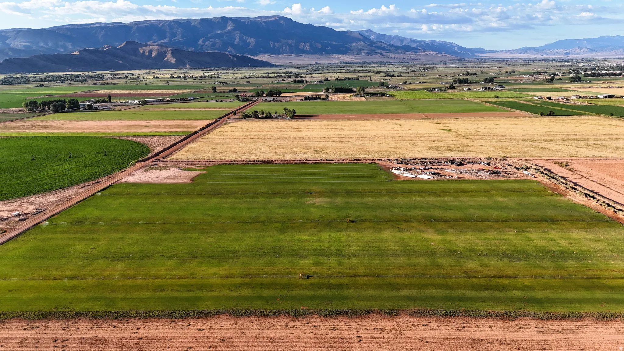 Expansive agricultural fields with varied crop stages, surrounded by distant mountains under a cloudy sky