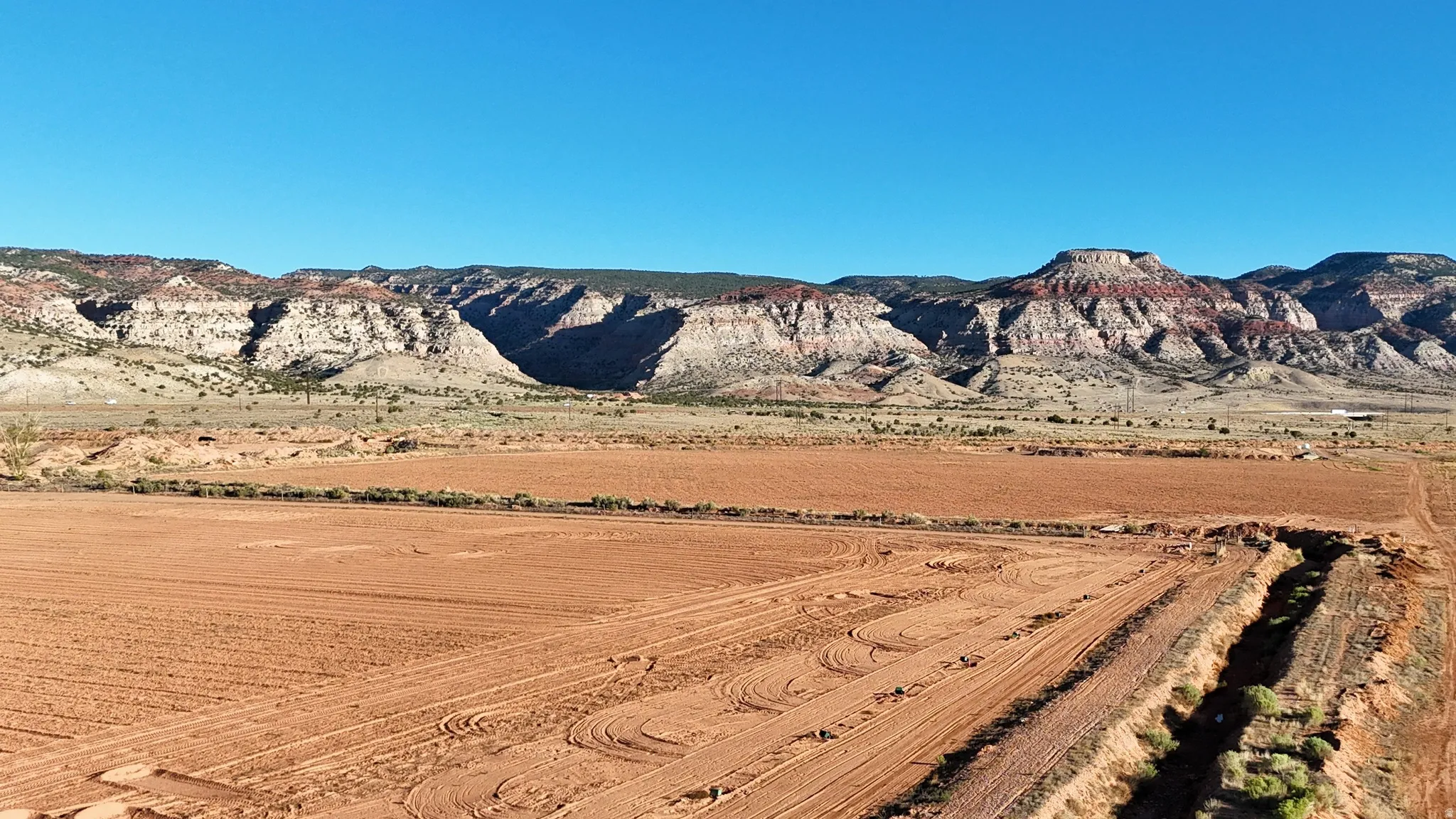 Expansive cleared land featuring rich red soil, with a visible ditch structure