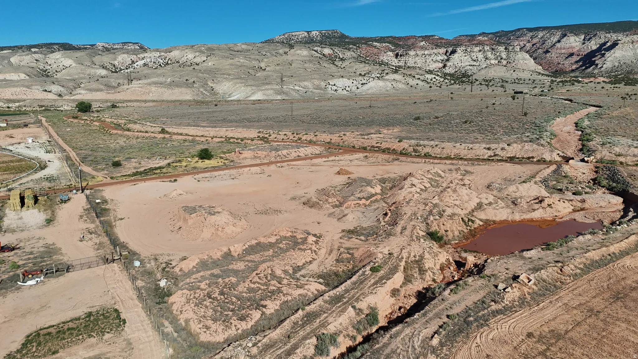 Expansive land parcel with graded terrain, a natural waterway, and distant mountain backdrops