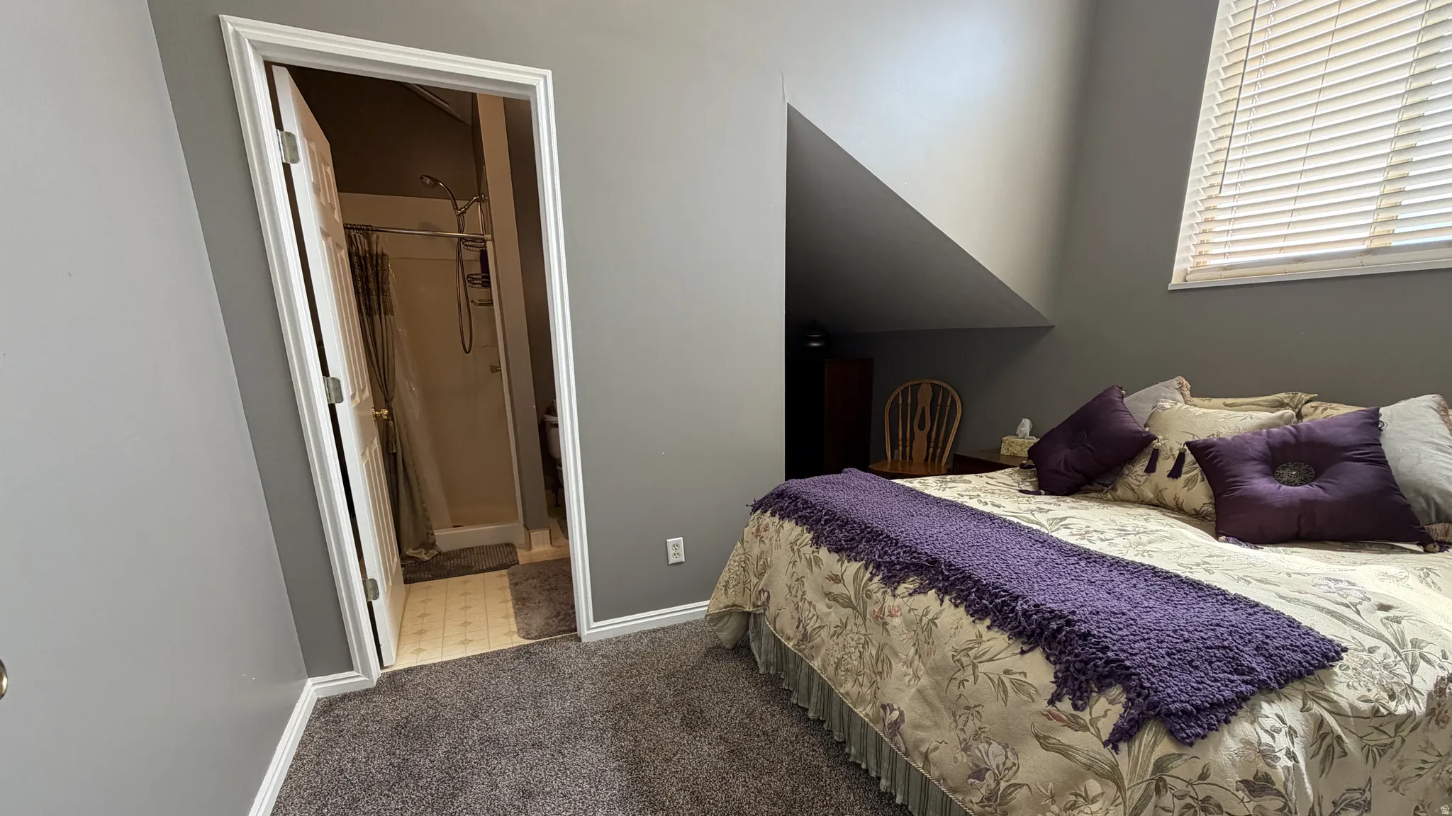 Carpeted room with an angled ceiling and a window featuring horizontal blinds