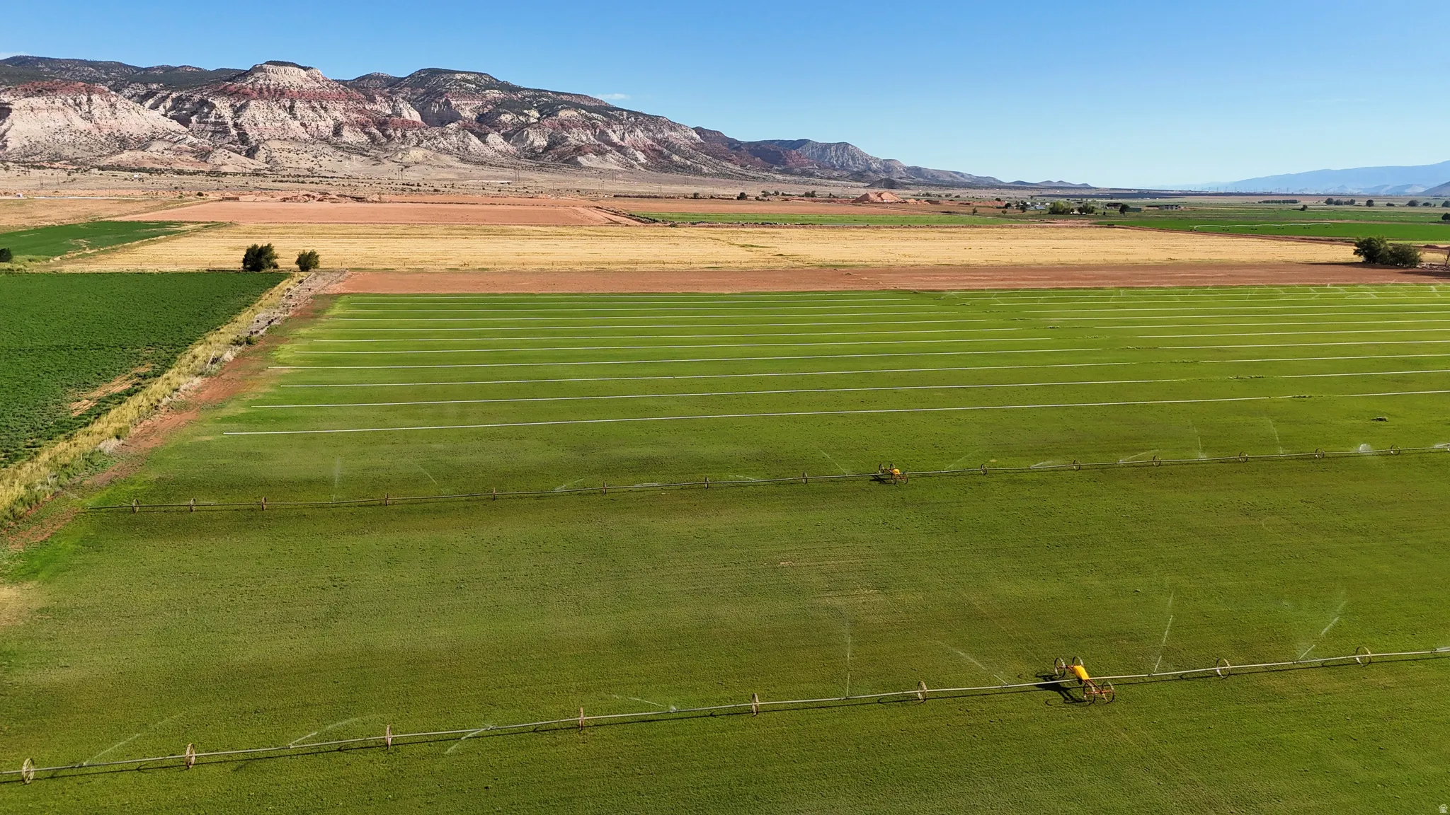 Expansive agricultural fields with active irrigation systems, bordered by varied terrain and distant mountains