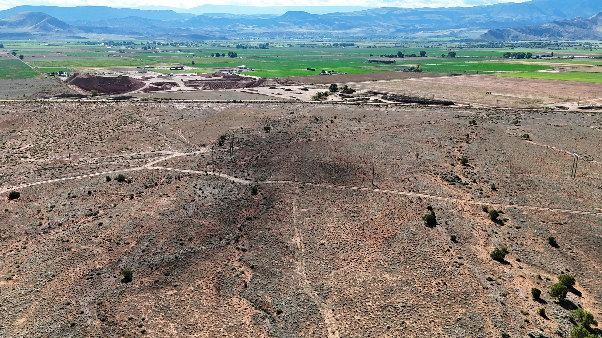 Expansive land parcel featuring natural desert flora, distant green fields, and surrounding mountains