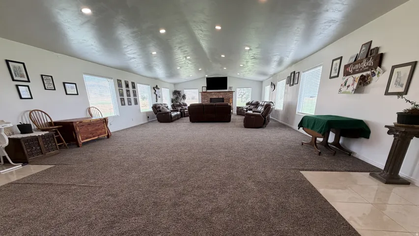 Spacious gathering room with recessed lighting, multiple windows, a stone-faced fireplace, and mixed flooring