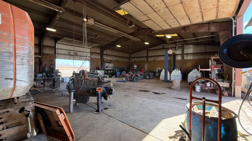 Spacious workshop featuring concrete flooring, multiple overhead doors, and high ceilings with exposed structural beams
