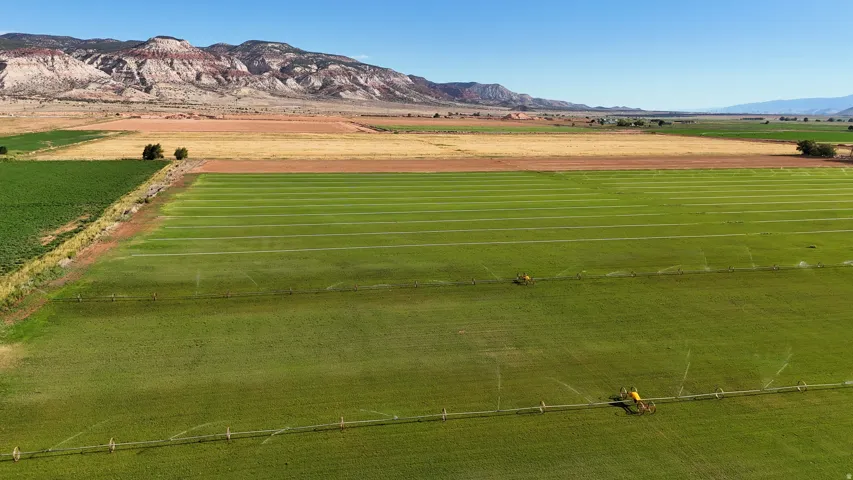 Expansive agricultural fields with active irrigation systems, bordered by varied terrain and distant mountains