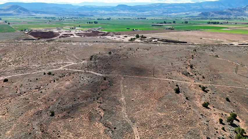 Expansive land parcel featuring natural desert flora, distant green fields, and surrounding mountains