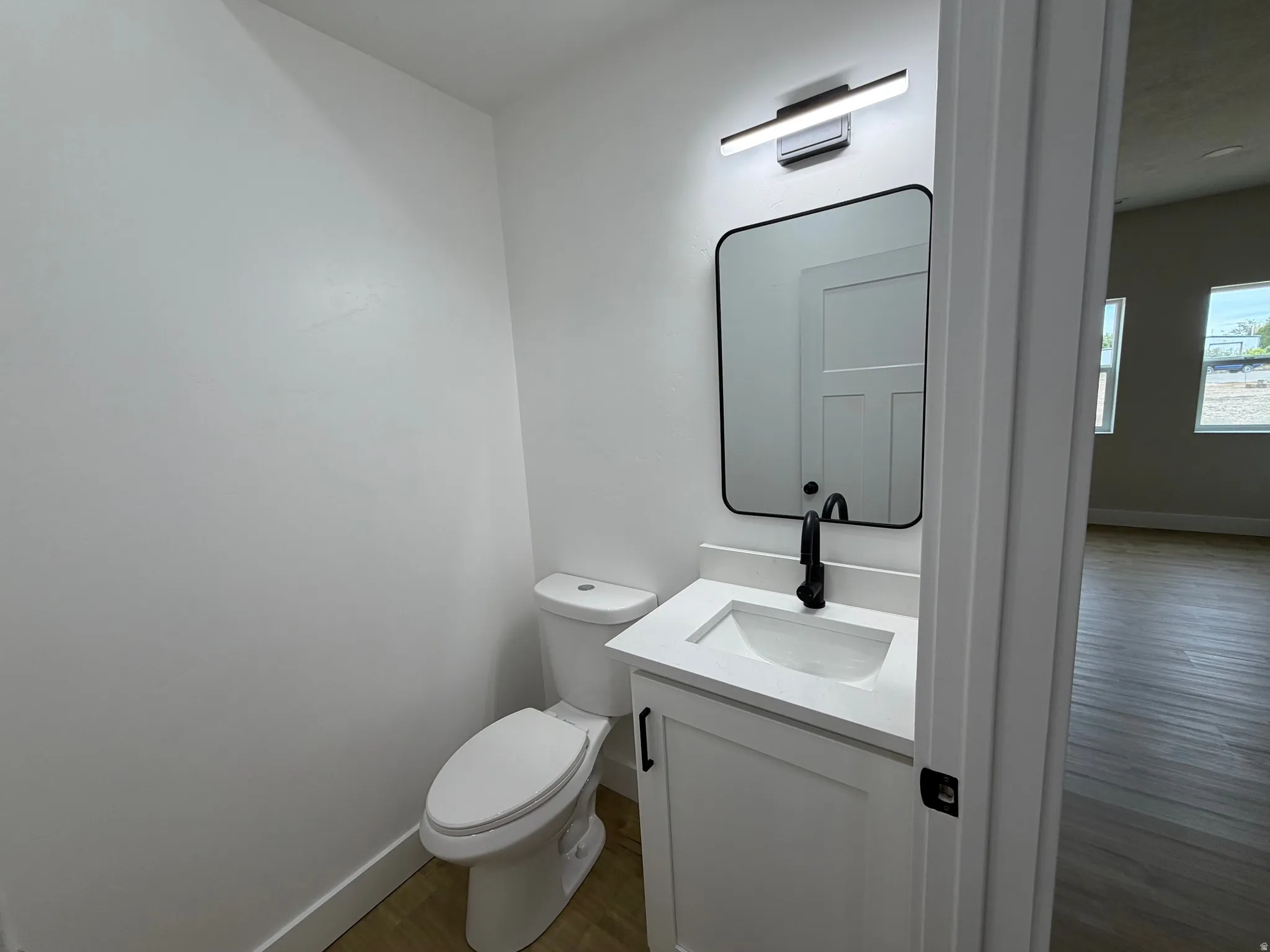 White vanity cabinet with integrated sink, black matte faucet, rectangular mirror, and overhead linear light fixture