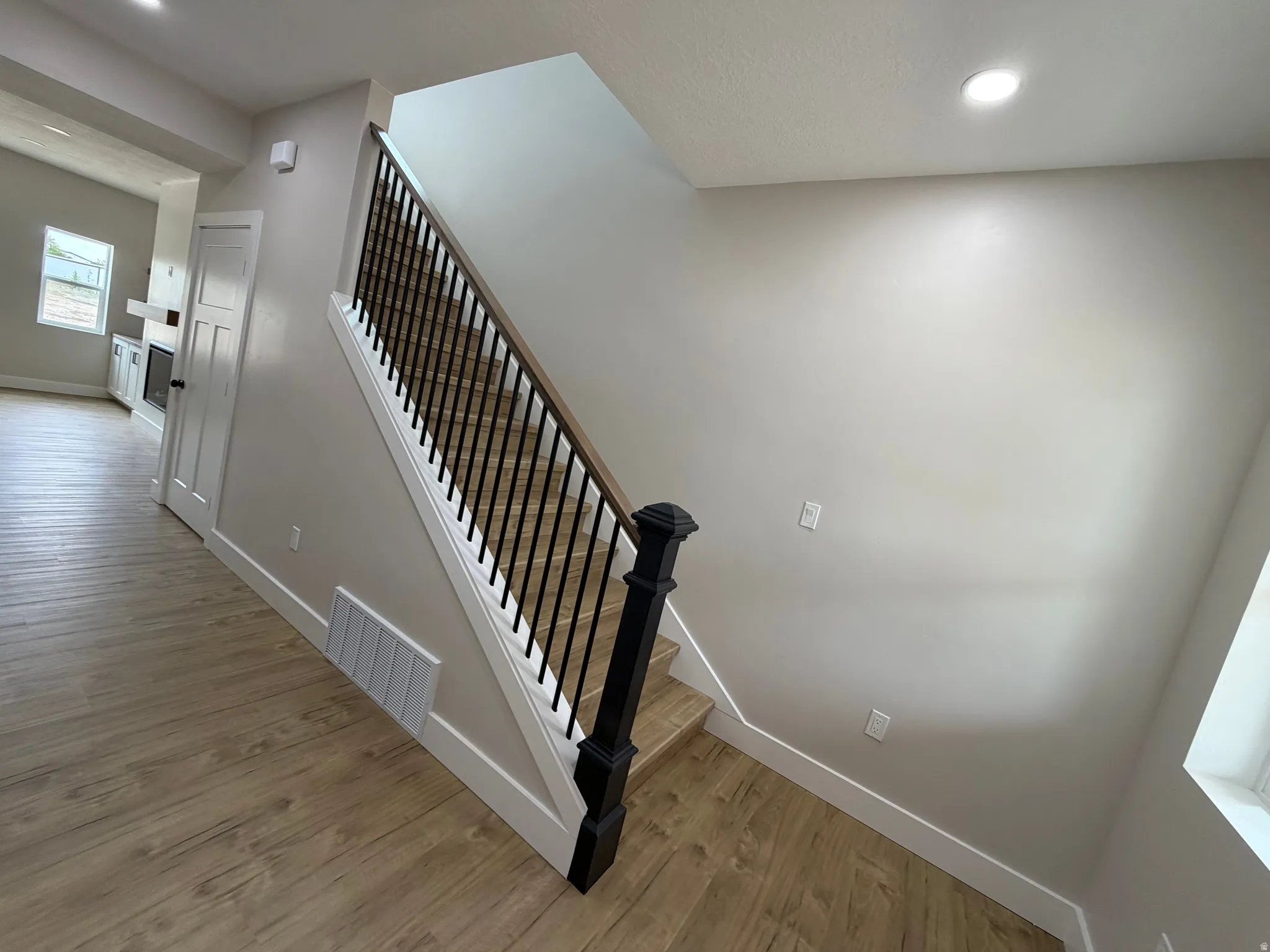 Wood-finish flooring throughout, with a staircase featuring black wrought iron balusters and a wood-finish handrail