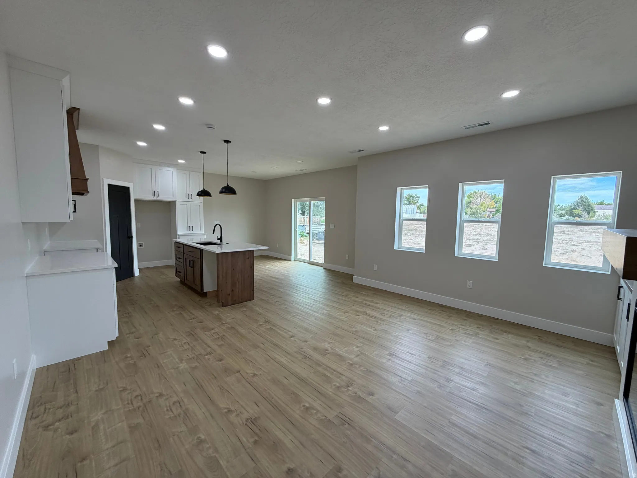 Open-concept interior featuring wood-finish flooring, recessed lighting, and a kitchen island with a built-in sink and pendant lights