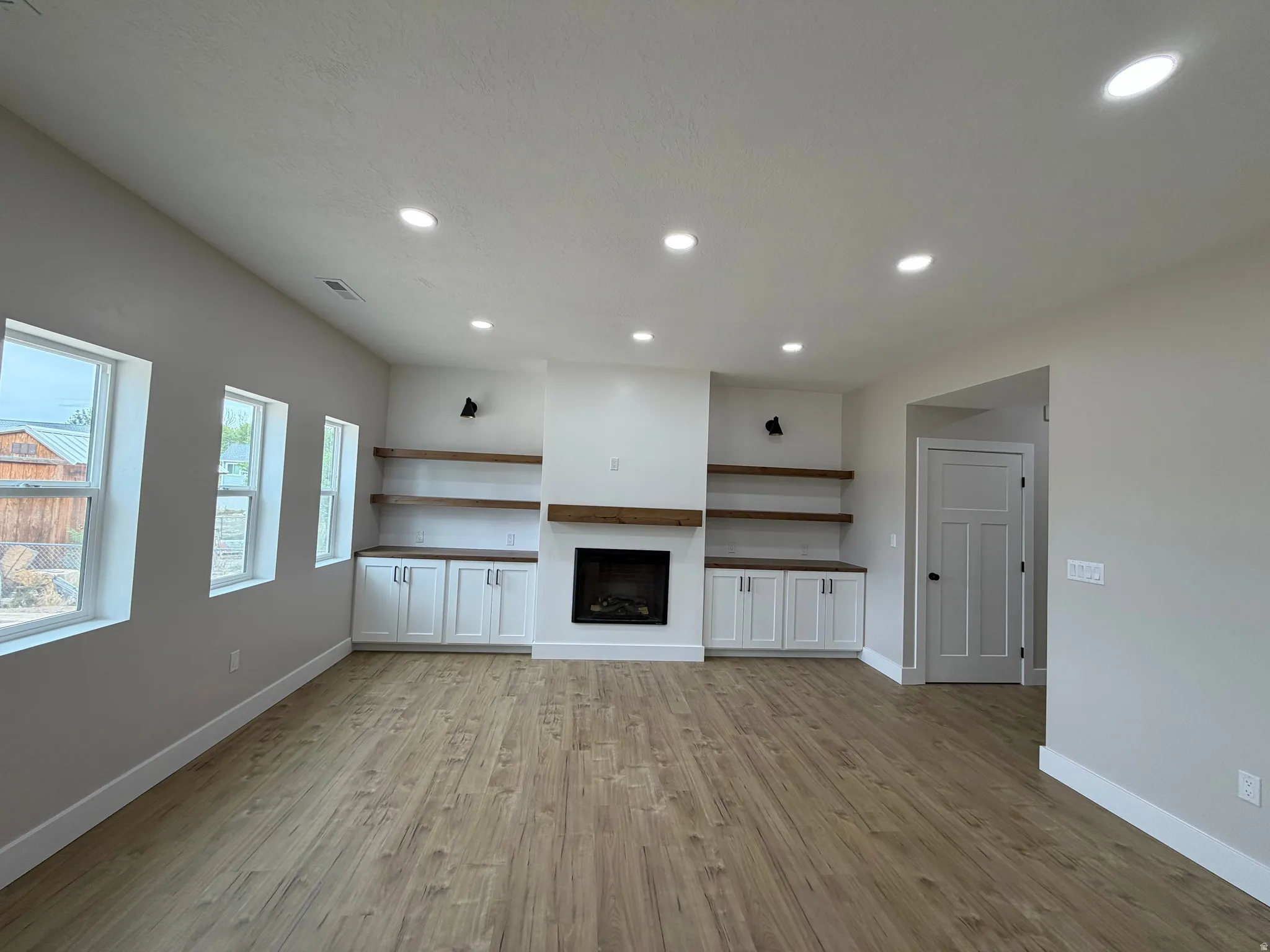 Recessed ceiling lighting, wood-finish flooring, built-in cabinetry with floating wood shelving, and a fireplace with a wood mantle