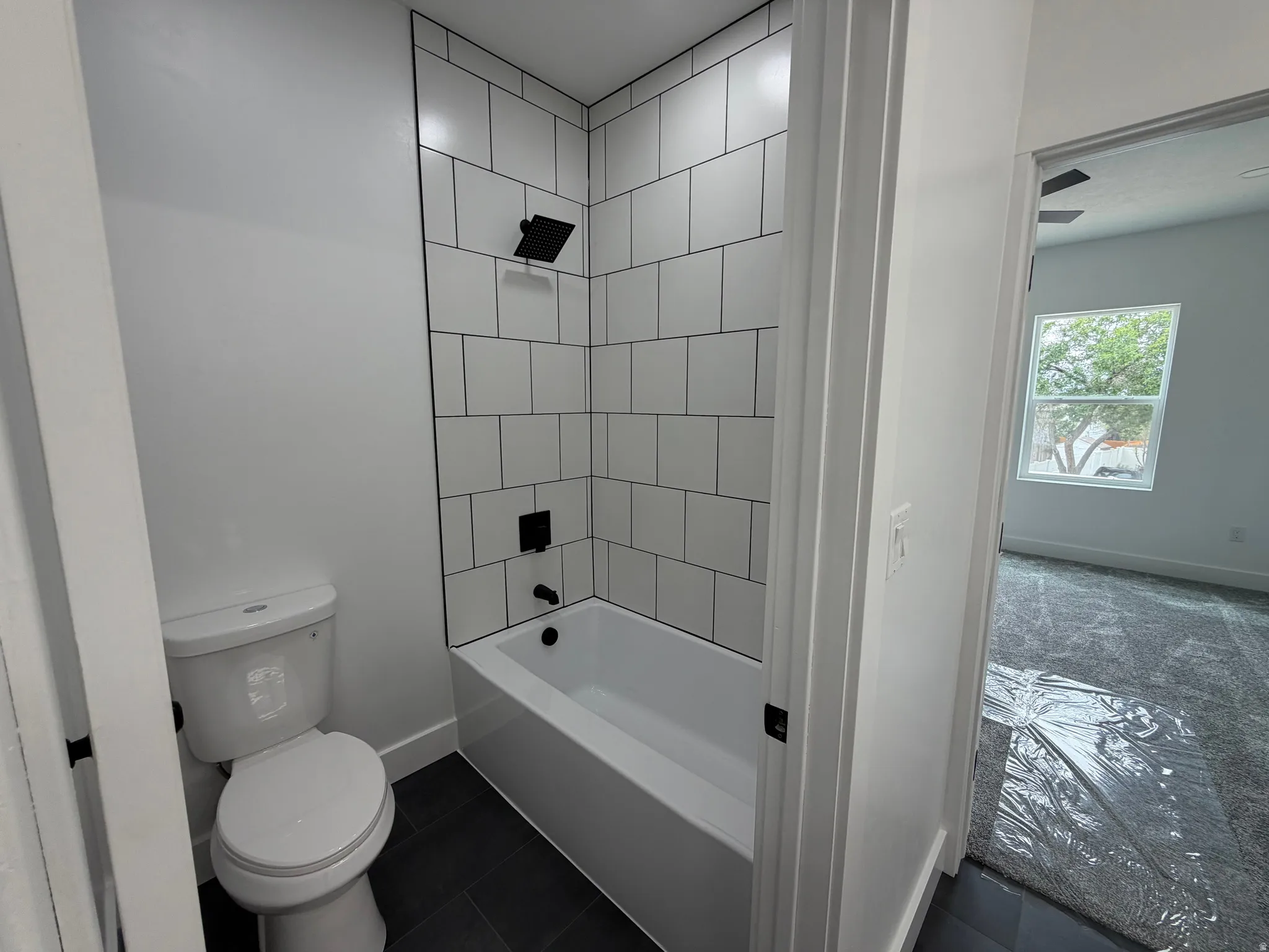 Master Bathroom - White subway tile shower surround with dark grout, matte black shower fixtures, white bathtub, dark floor tile, and white toilet