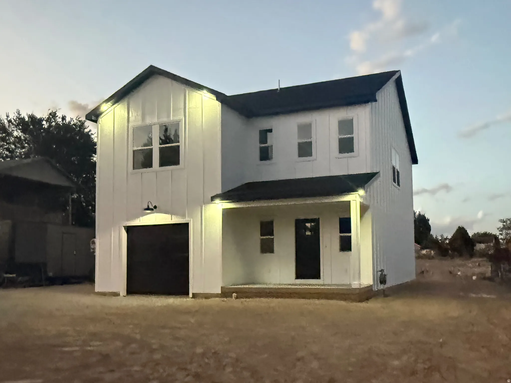Modern farmhouse exterior with white vertical siding, black garage door, covered front porch, and black-framed windows