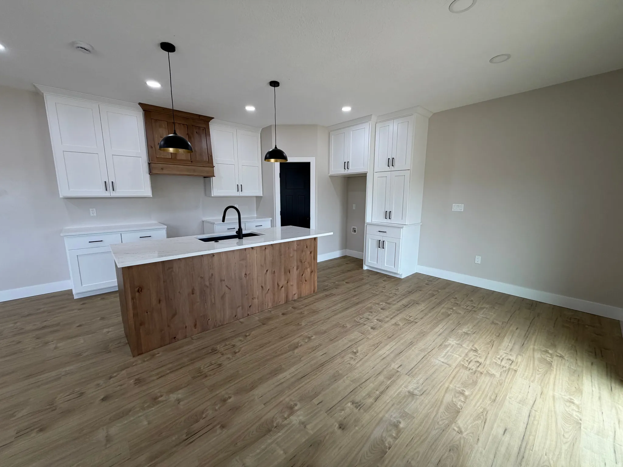White shaker cabinetry, wood-finish flooring, central island with integrated sink, recessed ceiling lighting, and pendant light fixtures