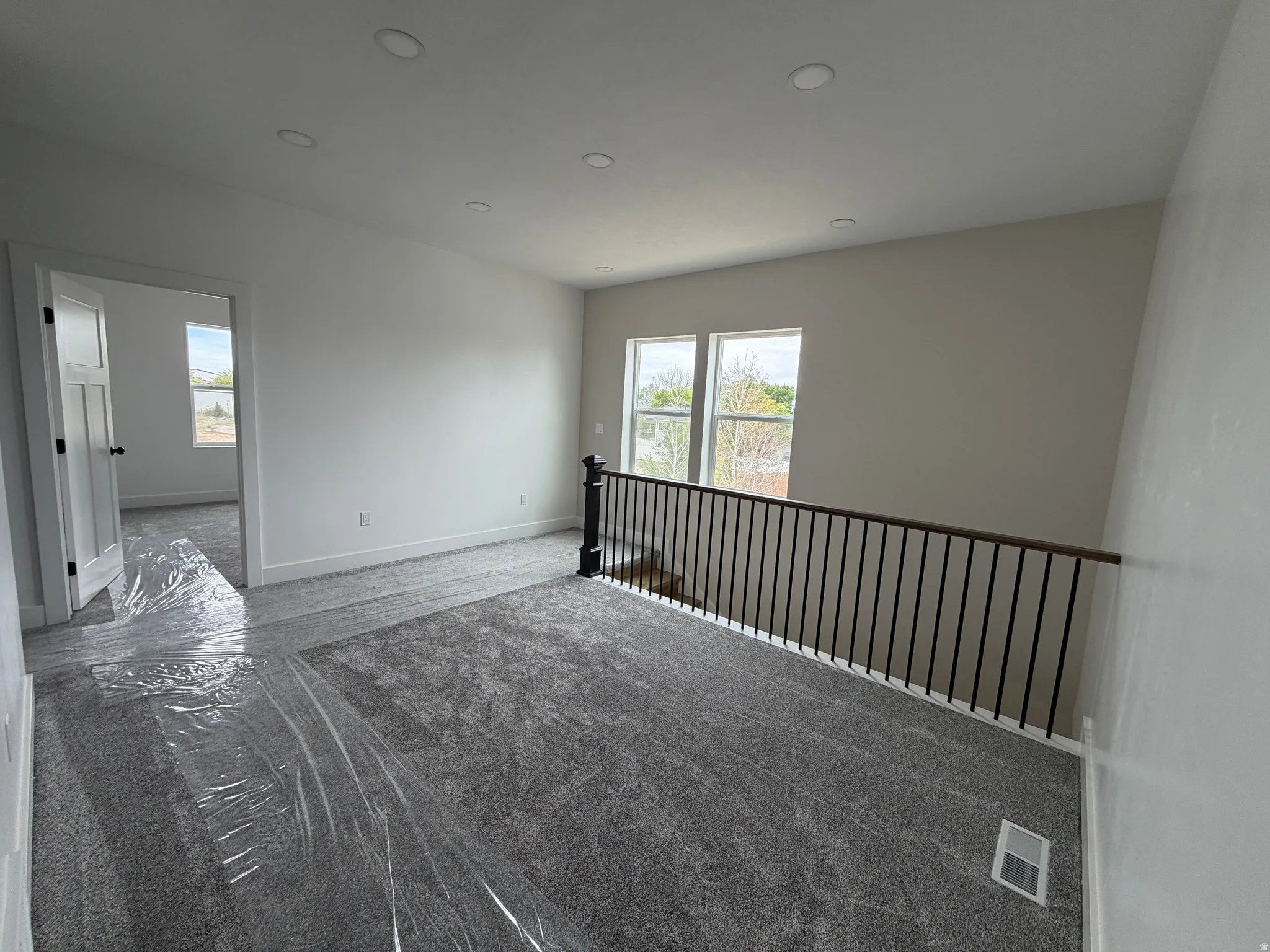 Recessed lighting, light gray carpeting, white walls, and a black wrought iron railing with a wood-finish top