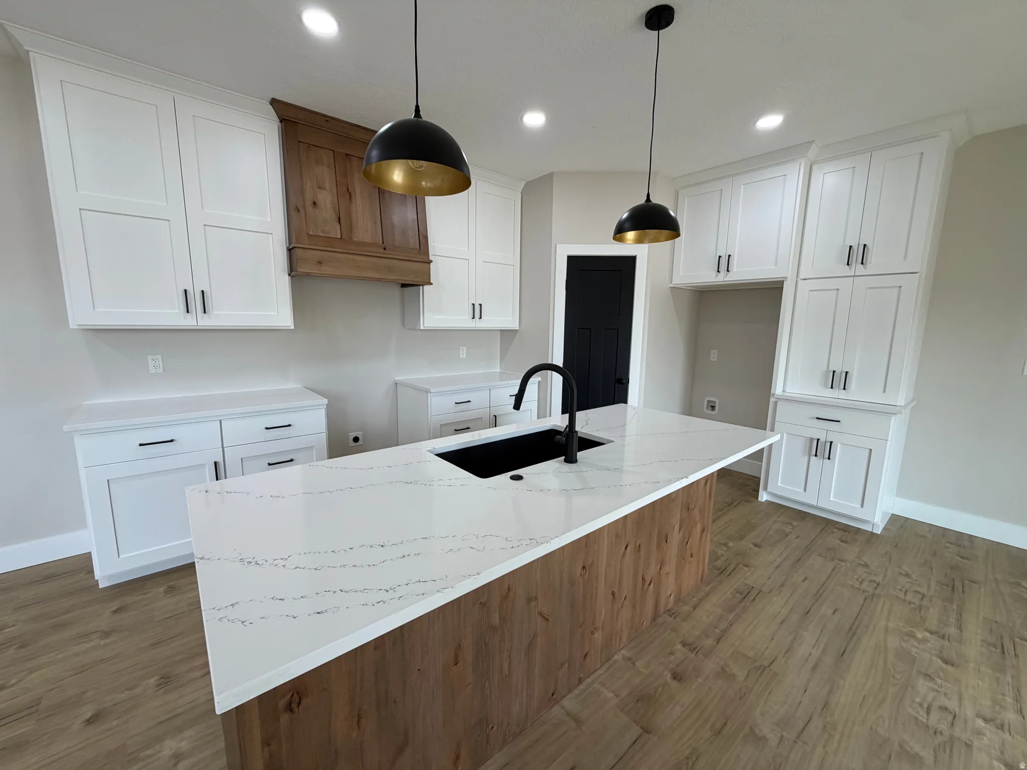 Kitchen featuring white shaker-style cabinetry, wood-finish flooring, a central island with a waterfall-edge countertop, and matte black pendant lighting