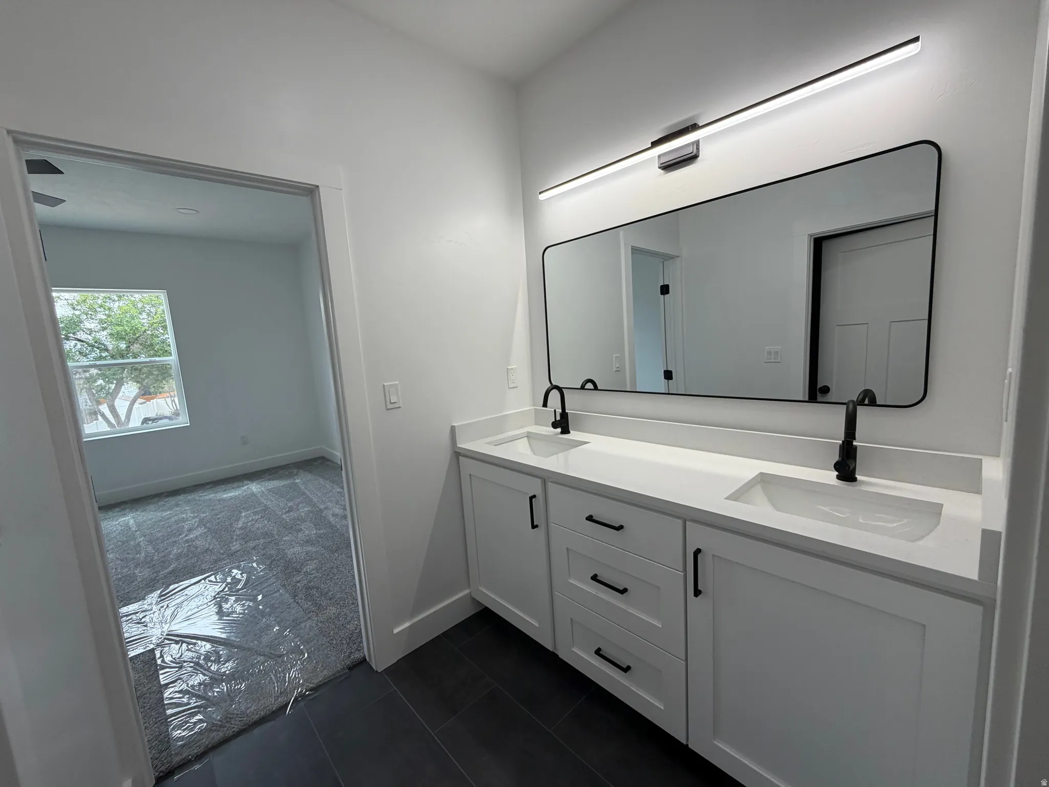 Master Bathroom - Double vanity with white cabinetry and integrated sinks, matte black hardware and fixtures, large framed mirror, and contemporary linear light fixture