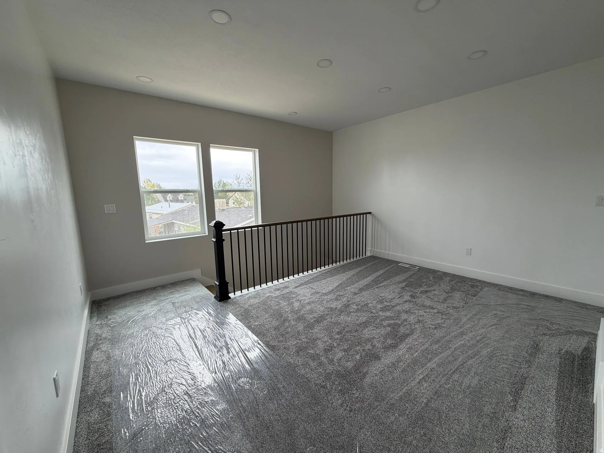 Open loft space featuring two windows, recessed lighting, a railing with black spindles, and grey carpeting