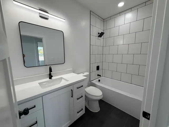 Upstairs Bathroom White subway tile shower surround with black grout, white vanity with an integrated sink, quartz countertop, and black hardware