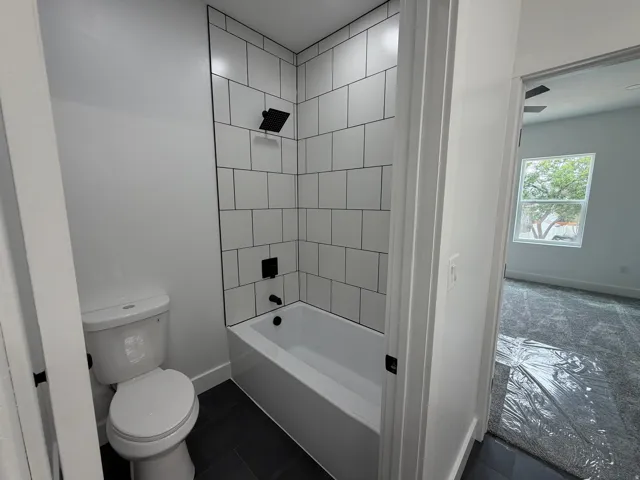 Master Bathroom - White subway tile shower surround with dark grout, matte black shower fixtures, white bathtub, dark floor tile, and white toilet