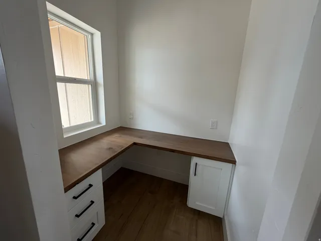 Built-in L-shaped desk with wood-finish countertop, white cabinetry with black hardware, and wood-finish flooring