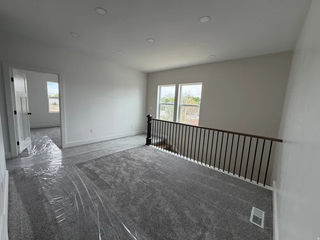 Recessed lighting, light gray carpeting, white walls, and a black wrought iron railing with a wood-finish top
