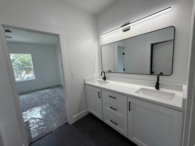 Master Bathroom - Double vanity with white cabinetry and integrated sinks, matte black hardware and fixtures, large framed mirror, and contemporary linear light fixture