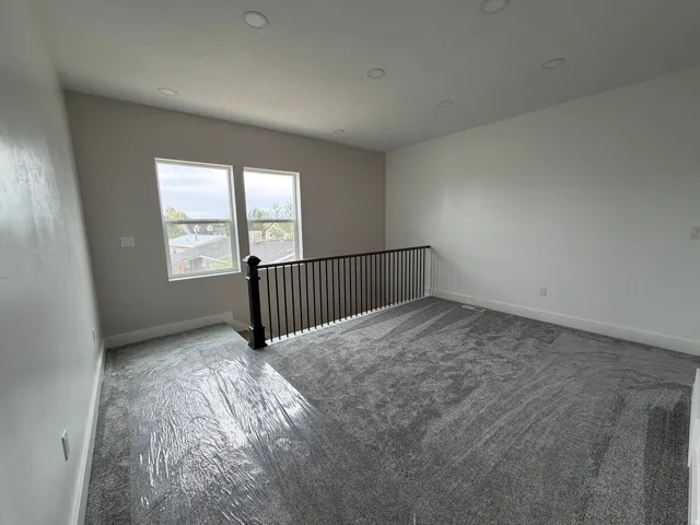 Open loft space featuring two windows, recessed lighting, a railing with black spindles, and grey carpeting