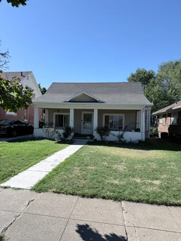 Gabled roofline with asphalt shingles, covered front porch with pillars, and concrete walkway