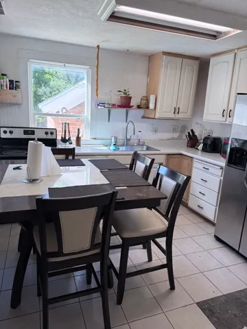 Kitchen featuring white upper cabinetry, light wood-finish lower cabinetry, white countertops, and stainless steel appliances