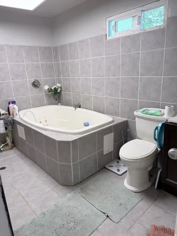Jetted tub with gray tile surround, gray tile flooring, and a fixed window