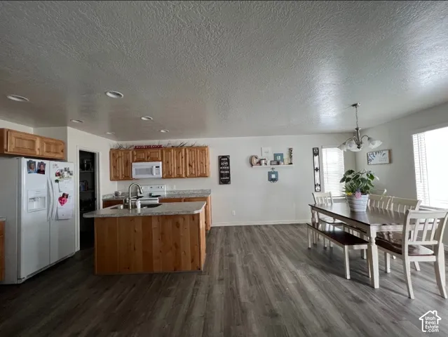 Kitchen and dining area featuring wood-finish flooring, recessed lighting, wood cabinetry, a kitchen island with sink, and a multi-light chandelier
