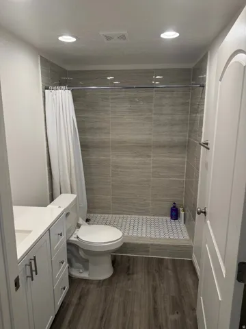 Shower with stone-finish wall tile, hex tile flooring, and a chrome shower rod
