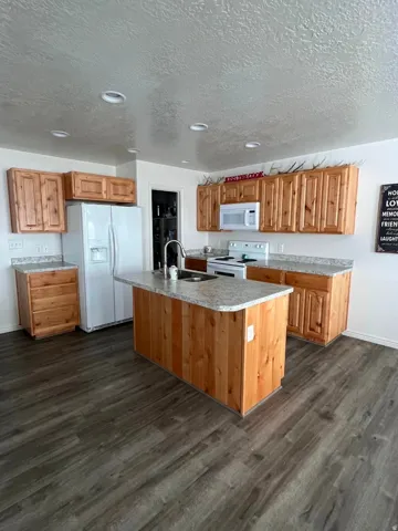 Kitchen featuring wood cabinetry, light-toned countertops, white appliances, recessed lighting, and wood-finish flooring