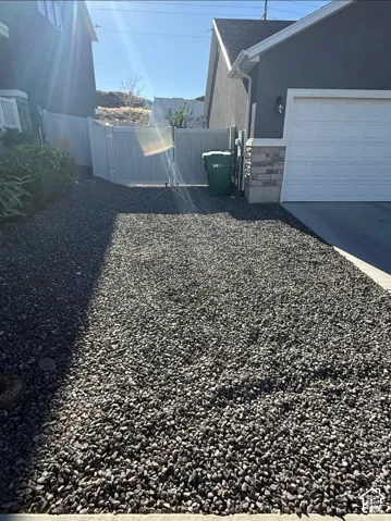 Gravel driveway with a white garage door, stone veneer accents, and a privacy fence