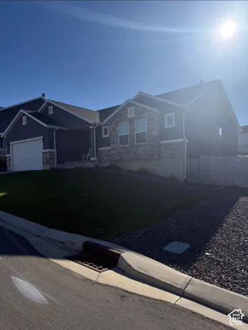 Two-story residence featuring a stone and siding facade, attached garage, and a sloped front lawn