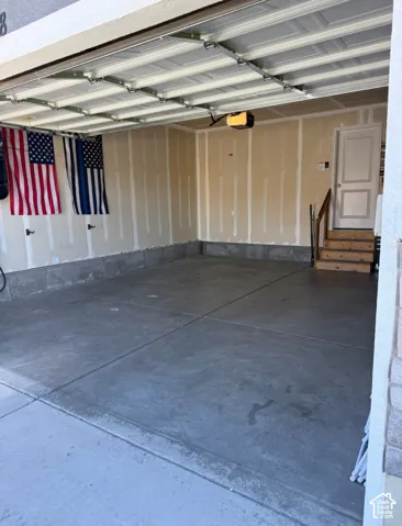 Two-car garage featuring a concrete floor, painted drywall, overhead garage door system, and an elevated interior entry door with wood-finish stairs