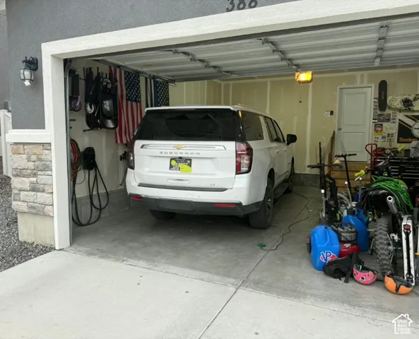 Attached garage with a concrete floor, finished interior walls, overhead lighting, and a service door