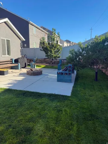 Expansive backyard featuring a manicured lawn, concrete patio, and a built-in fire pit